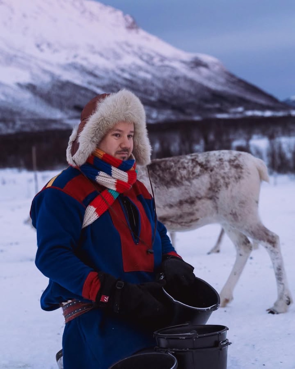 Jon Mikkel in gákti with a reindeer behind him